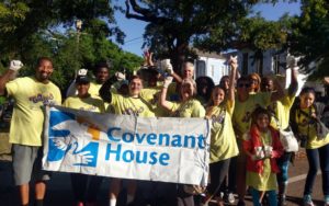A group of sixteen people in matching t-shirts holding up a Covenant House banner.