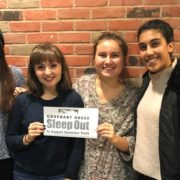 Four teenage girls stand smiling in front of a brick wall. The middle two girls hold each side of a piece of paper reading "Covenant House Sleep Out to Support Homeless Youth".