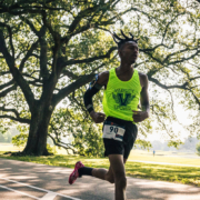 Jakiya, a male Covenant House resident wearing a neon green event tank top, is mid-stride as he runs through the beautiful greenery of the Audubon.