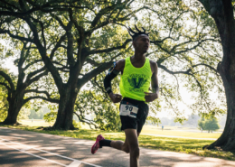 Jakiya, a male Covenant House resident wearing a neon green event tank top, is mid-stride as he runs through the beautiful greenery of the Audubon.