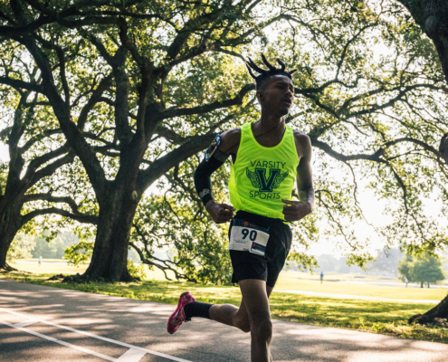 Jakiya, a male Covenant House resident wearing a neon green event tank top, is mid-stride as he runs through the beautiful greenery of the Audubon.