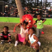 Four young children smile as they pose in front of a red art piece