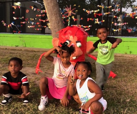 Four young children smile as they pose in front of a red art piece