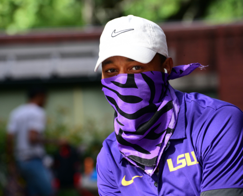 Man poses for camera wearing LSU polo and purple tiger neck gaiter