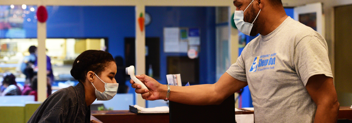 Resident gets their temperature taken at Covenant House reception desk. Both people wearing masks