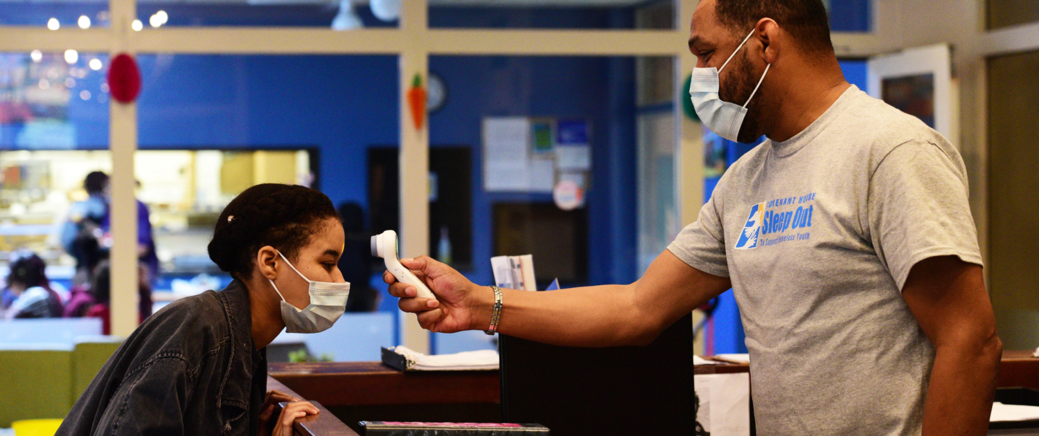 Resident gets their temperature taken at Covenant House reception desk. Both people wearing masks