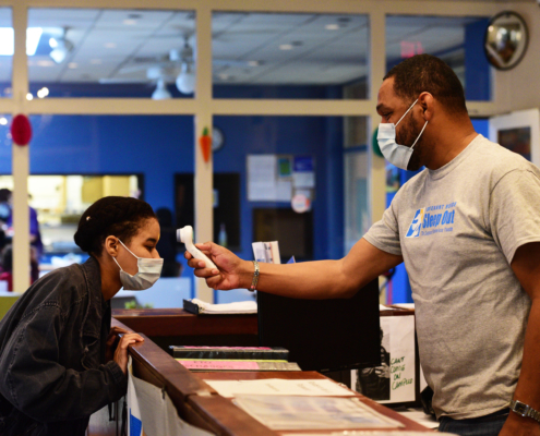 Resident gets their temperature taken at Covenant House reception desk. Both people wearing masks