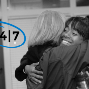 Two women hugging with "24/7" circled to their left