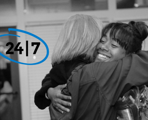 Two women hugging with "24/7" circled to their left