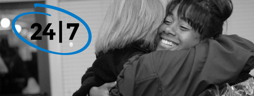 Two women hugging with "24/7" circled to their left