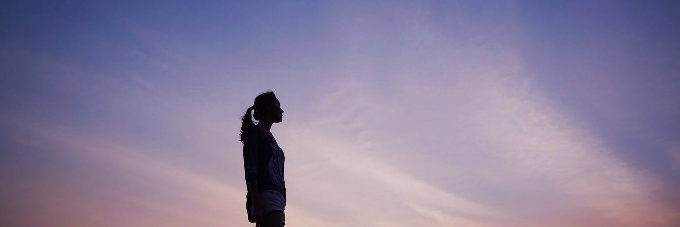 Woman standing silhouetted by purple sky background