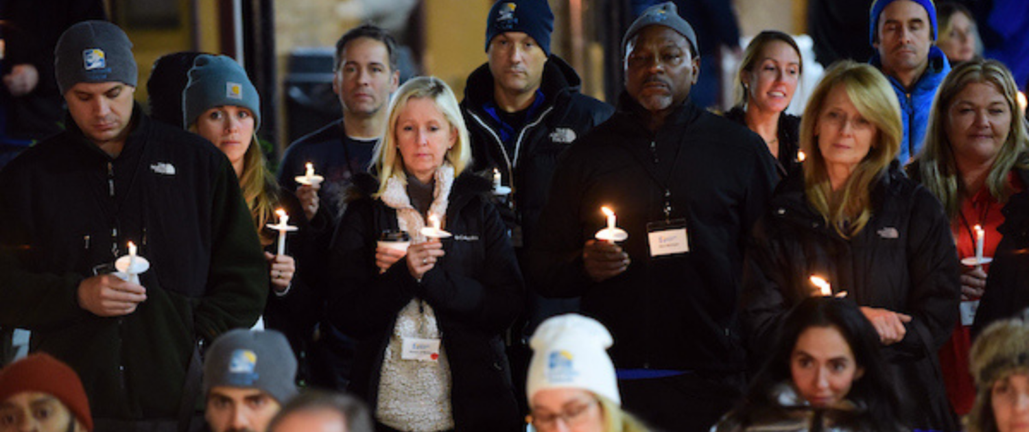 Group of adults standing together, somberly holding candles.