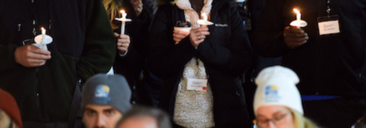 Group of adults standing together, somberly holding candles.