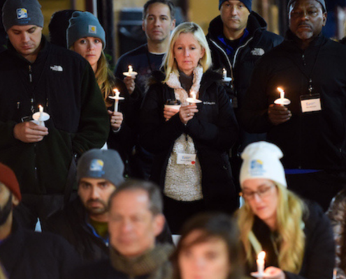 Group of adults standing together, somberly holding candles.