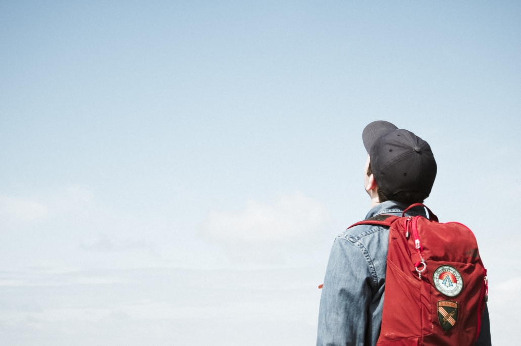 A boy with a red backpack looks up to the sky.