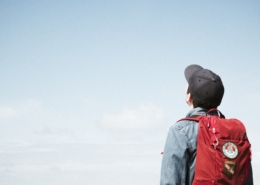 A boy with a red backpack looks up to the sky.