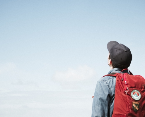 A boy with a red backpack looks up to the sky.